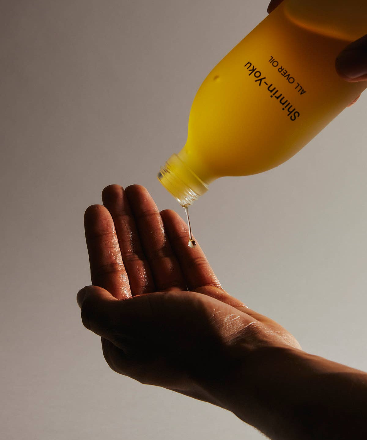 Yellow bottle pouring liquid into a hand against a neutral background