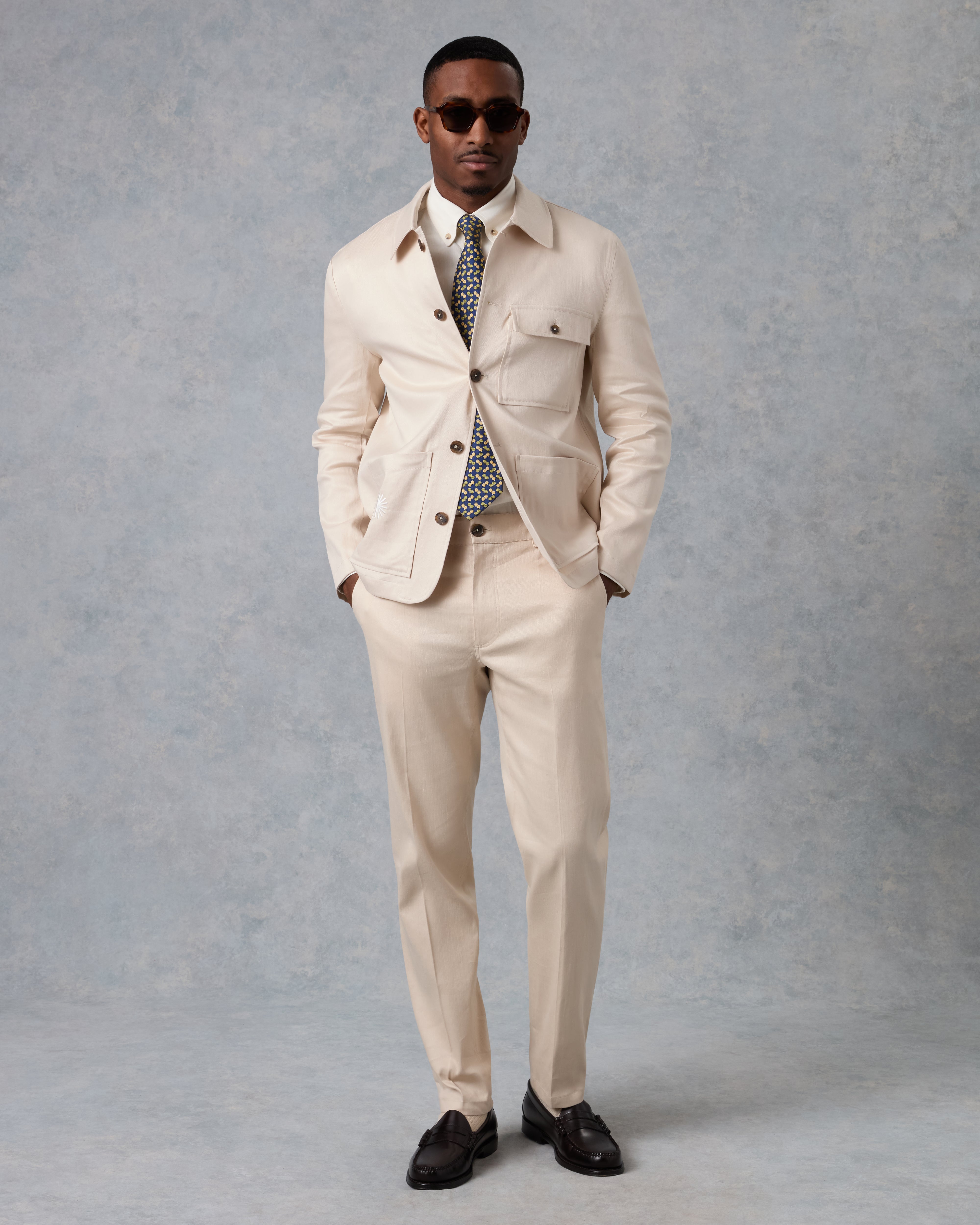 Man wearing a beige suit with sunglasses on a gray background